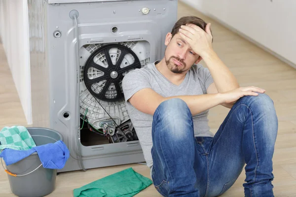 Bitkin Genç Adam Bozuk Çamaşır Makinesinin Yanında Oturuyor — Stok fotoğraf