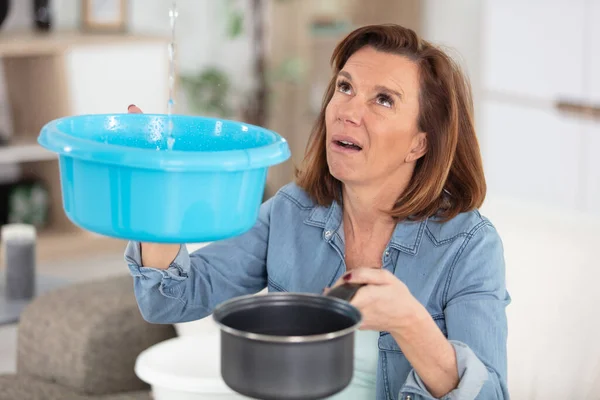 Worried Woman Holding Bucket While Water Droplets Leak Ceiling — Stockfoto