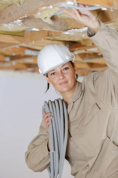 在屋顶空间安装电缆的女建筑工人 — 图库照片