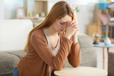 woman kneeling in prayer in the living room clipart