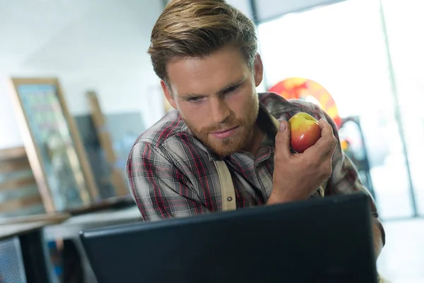 Foto Van Mannelijke Werknemer Met Appel Fruit Controleren Laptop — Stockfoto