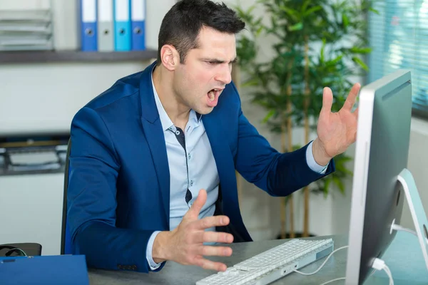 オフィスのデスクでコンピューターに向かって叫んでいる男に — ストック写真