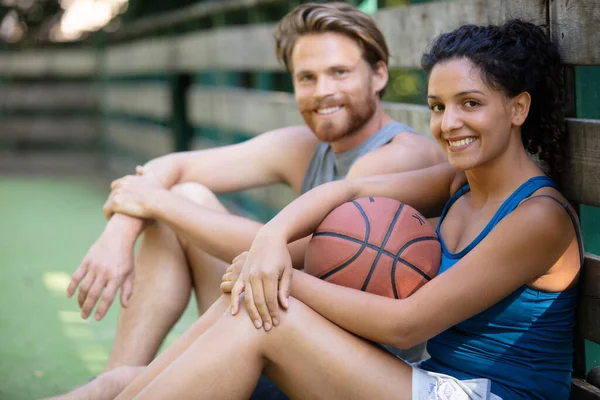一对年轻夫妇坐在篮球场上 球着地 — 图库照片