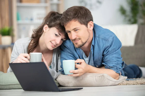 幸せなカップルチェックノートパソコンのオンラインコンテンツ保持コーヒーカップ — ストック写真