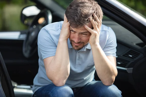 portrait of stressed man sitting on his car