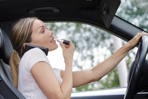 女性は車の運転中に口紅をつけて電話で話し — ストック写真