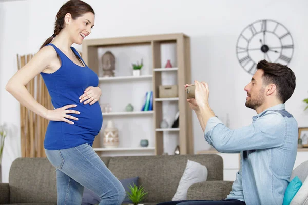 快乐的丈夫用智能手机给他怀孕的妻子拍照 — 图库照片