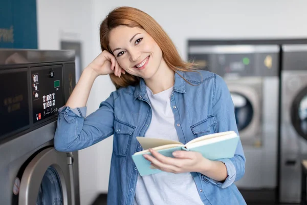 Beautiful Young Woman Reading Book While Doing Laundry — Stock Photo, Image