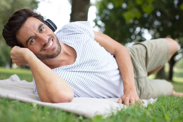 ヘッドフォンを装着したハンサムな男が草の上に横たわっています — ストック写真