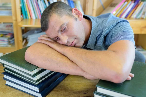 Unatkozó Ember Támaszkodik Halom Könyvet Könyvtárban — Stock Fotó