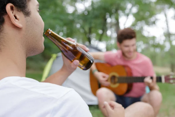 Dwóch Młodych Mężczyzn Przy Namiocie Grających Gitarze Pijących Piwo — Zdjęcie stockowe