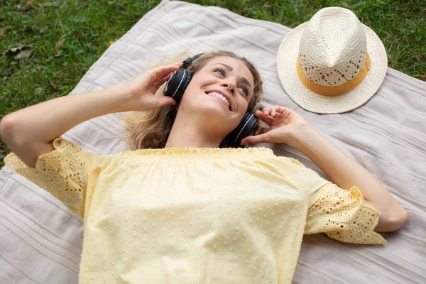 草の上で音楽を聴いている若い美しい女性は — ストック写真
