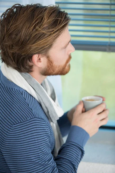 ハンサムな男が窓のそばに立ってコーヒーカップを持っていて — ストック写真