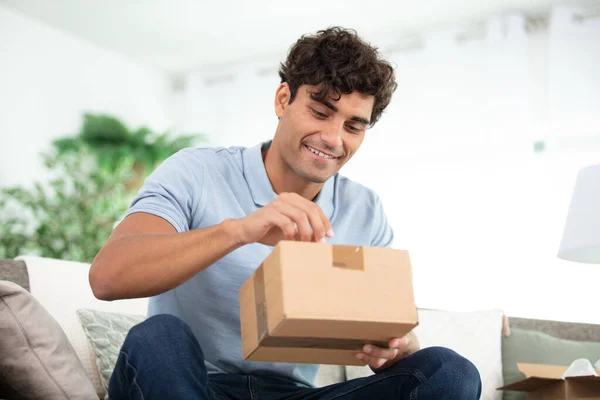 Handsome Young Man Opening Parcel While Sitting Sofa — Stock Photo, Image