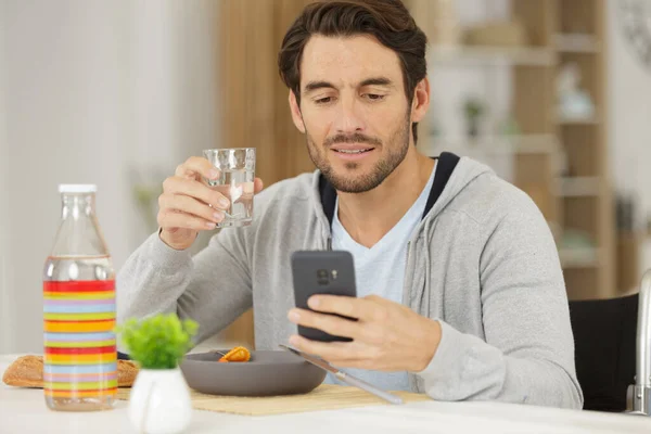 Uomo Sulla Sedia Rotelle Utilizzando Smartphone Mentre Mangia Pasto — Foto Stock