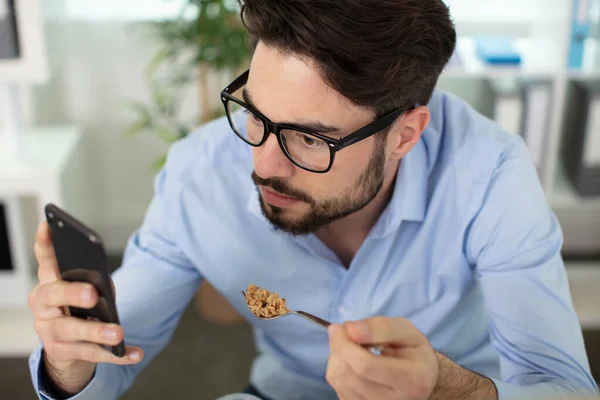 帅哥在厨房里用智能手机吃麦片 — 图库照片