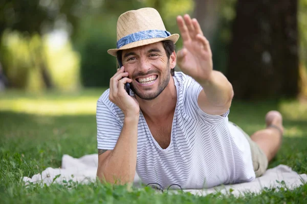 英俊的男人躺在草地上 一边打电话一边挥手 — 图库照片
