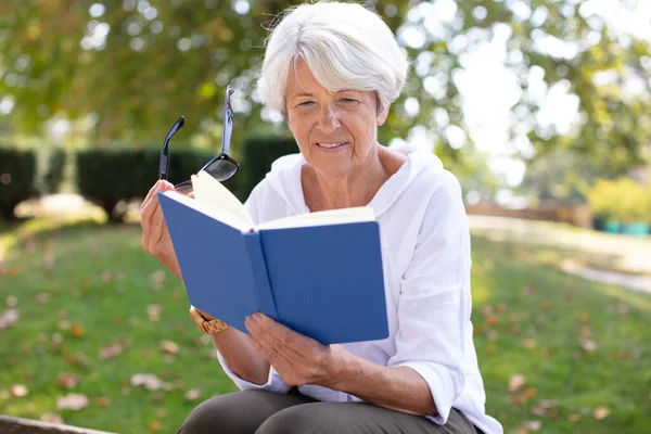 一个成熟的金发女人在花园里看书 — 图库照片