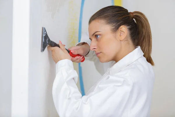 女性工業用絵画の見習いスクレーピング壁 — ストック写真