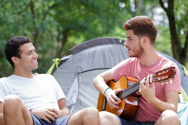 年轻人坐在帐篷周围弹奏吉他 — 图库照片