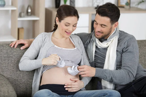 快乐的怀孕夫妇抱着婴儿鞋在沙发上 — 图库照片