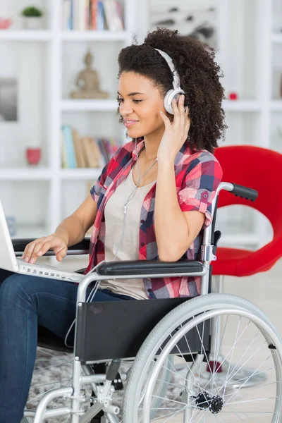 ノートパソコンとヘッドフォンを持った車椅子の若い女性は — ストック写真