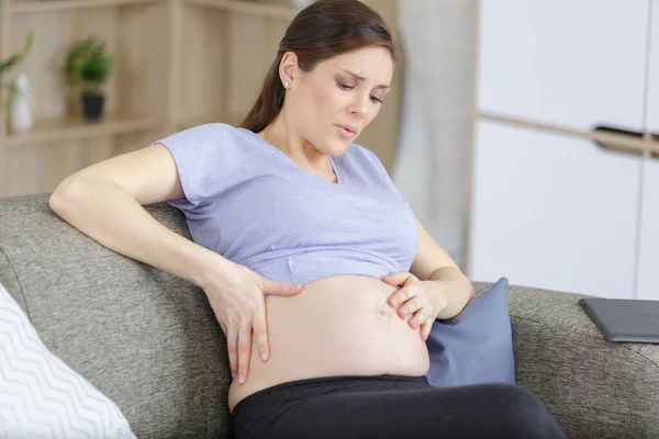 痛苦的孕妇坐在家里的沙发上 — 图库照片