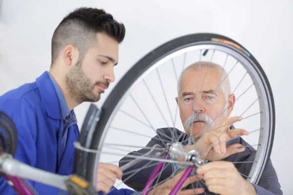 Sênior Conversando Com Aprendiz Enquanto Fixa Roda Bicicleta — Fotografia de Stock