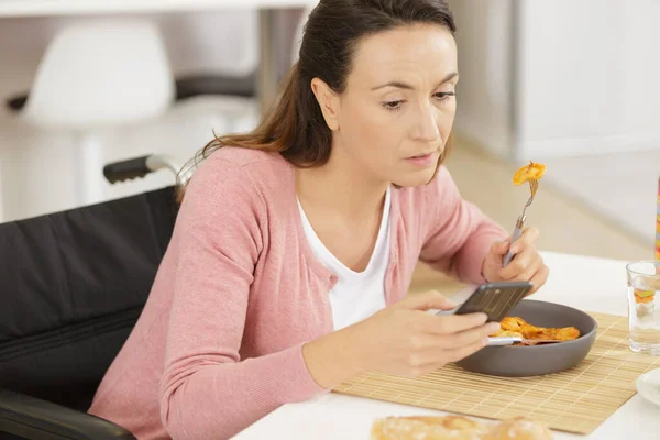 Tekerlekli Sandalyedeki Kadın Telefon Kullanırken Yemek Yiyor — Stok fotoğraf