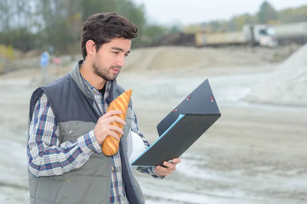 Man Eating Baguette Looking File Construction Site — Stock Photo, Image