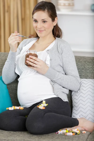チョコレートを食べるのを楽しんで自宅で笑顔の妊婦 — ストック写真