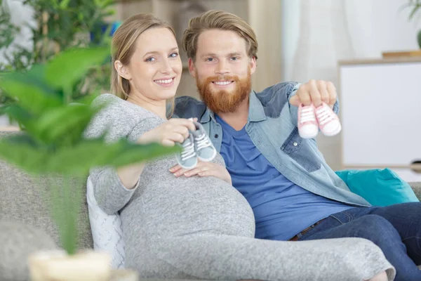 赤ちゃんの靴を見せる若い妊婦のカップル — ストック写真