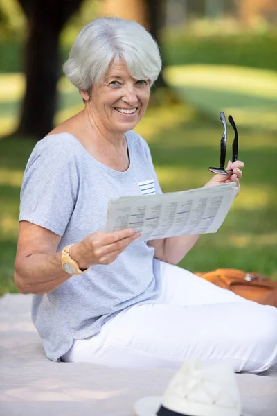 年长的快乐女人坐在公园的草地上 — 图库照片