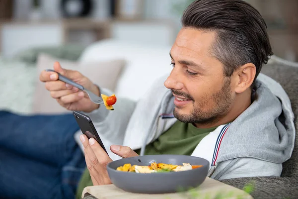 Άνθρωπος Στον Καναπέ Χρησιμοποιώντας Smartphone Ενώ Φαγητό — Φωτογραφία Αρχείου