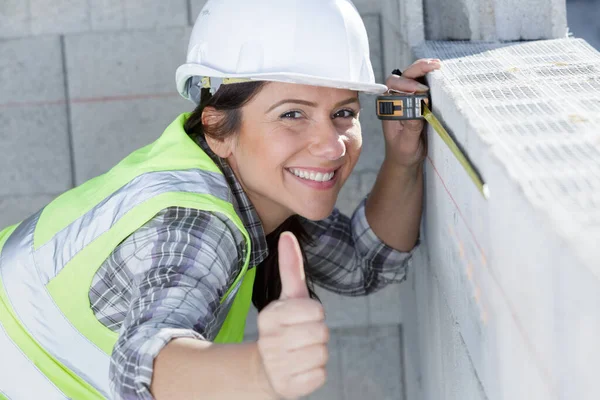 壁を測定しながら親指を示す幸せな女性ビルダー — ストック写真