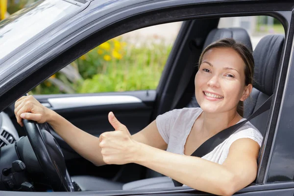 年轻的女司机坐在方向盘后面做着竖起大拇指的手势 — 图库照片