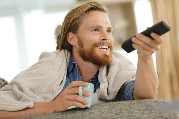 stock image happy young man with tv remote control on sofa