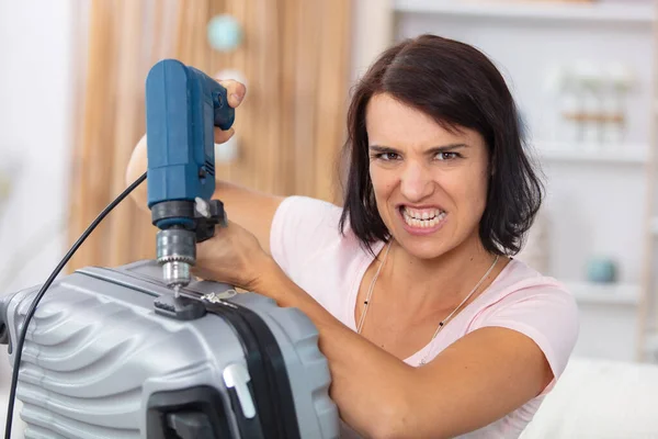 生气的女人用钻头打开锁好的手提箱 — 图库照片