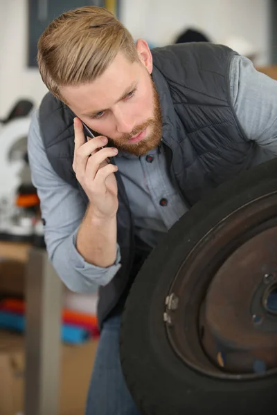 Człowiek Mechanik Trzyma Telefon Komórkowy Patrząc Opony Samochodu — Zdjęcie stockowe