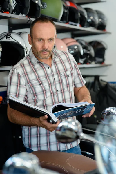 オートバイのショールームのカタログを見ている男 — ストック写真