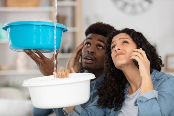 emotional young couple collecting water leaking from ceiling