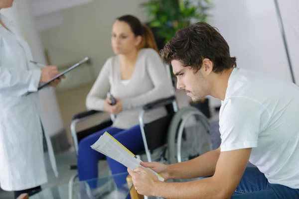 看護師が障害のある女性と話しながら クリニックで読書する男 — ストック写真