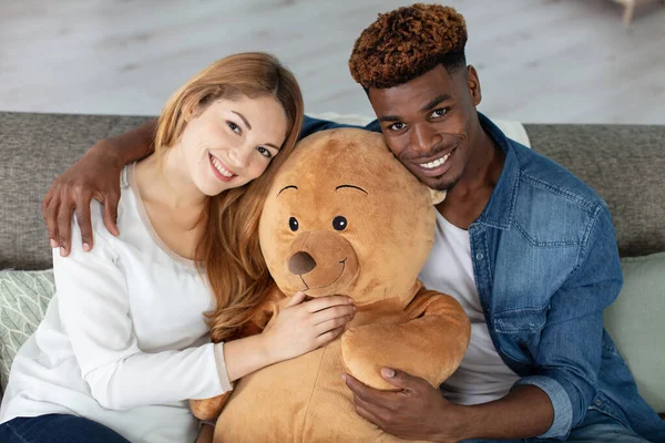 笑着的女人和丈夫 大玩具熊躺在沙发上 — 图库照片