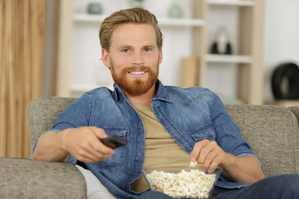 happy young man eating popcorn while sitting on a couch