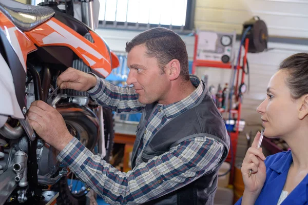男子在摩托车车间帮助女客户修理自行车 — 图库照片