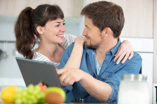 young couple with digital tablet sitting in kitchen