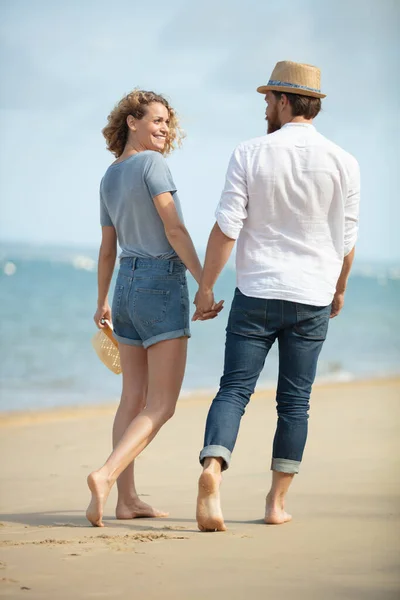幸せなカジュアルな若いカップルはビーチで手を握っています — ストック写真