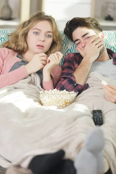 young couple with popcorn watching scary movie on tv