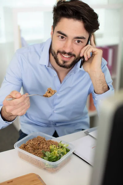 Stock image young business man talking on the phone while eating