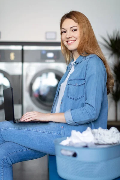 洗衣服时使用手提电脑完成多项任务的女人 — 图库照片